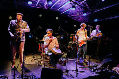 Muzikanten spelen op een podium met verschillende instrumenten tijdens een live optreden.