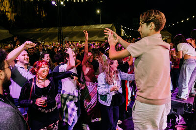 Mensen dansen en genieten van een optreden op een levendig festival, met licht en een feestelijke sfeer.