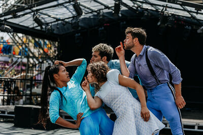 Groep dansers in kleurrijke kleding voeren een expressieve choreografie uit op een podium.