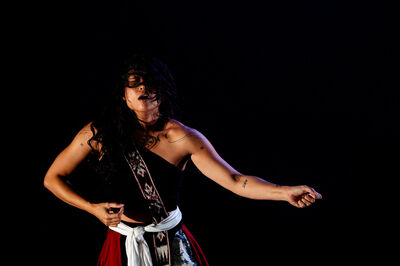 Vrouwelijke performer in een zwarte outfit danst expressief op een podium met een donkere achtergrond.