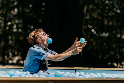 Een jongeman jongleert met blauwe ballen in een zwembad gevuld met plastic ballen.