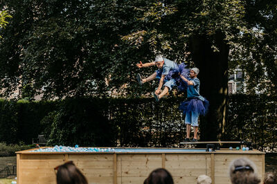 Twee performers voeren een act op een podium uit, terwijl een publiek op de voorgrond toekijkt.