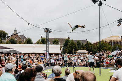 Een artiest voert een sprongetje uit op een touw boven een grote menigte tijdens een circusvoorstelling.