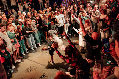 Een enthousiaste menigte kijkt toe terwijl dansers optreden in een straatfeest-setting.