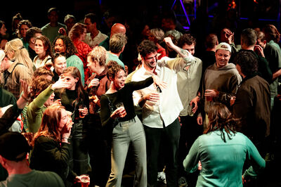 Groep mensen dansend en socialiserend tijdens een feest in een drukke zaal met sfeerverlichting.