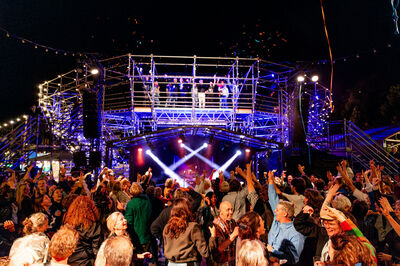 Een drukke concertlocatie met een enthousiast publiek dat danst onder kleurrijke verlichting.