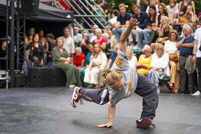 Een breakdancer voert een acrobatische beweging uit op een podium terwijl een publiek toekijkt.