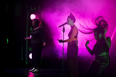 Drie artiesten performen op een podium met paarse en groene verlichting en rook.