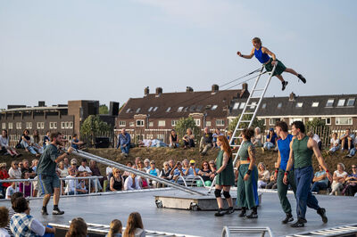 Vijf artiesten voeren een circusact uit met een ladder en een springer, terwijl het publiek toekijkt.