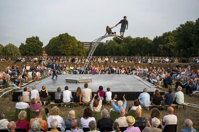 Een acrobatische act op een openlucht podium met een groot publiek dat toekijkt.