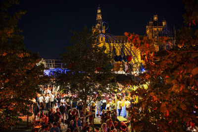 Drukke avond met mensenmenigte tijdens een evenement in een stadspark, verlicht door feestverlichting.