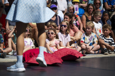 Een vrouw in een blauwe jurk danst voor een publiek van kinderen op een evenement.