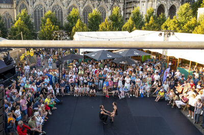 Een drukke openluchtvoorstelling met een dansduo voor een enthousiast publiek in een stad. Achtergrond met een kathedraal.