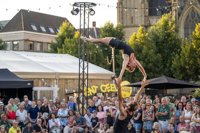 Een acrobatisch duo presteert een stunt tijdens een buitenvoorstelling voor een enthousiast publiek.