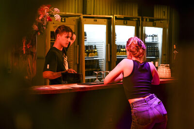 Bartender en klant in een bar, converserend bij de bar met kleurrijke verlichting op de achtergrond.