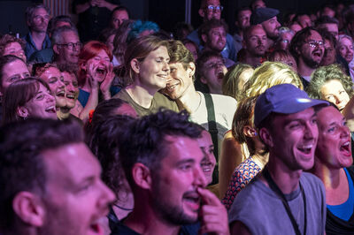 Een enthousiaste menigte geniet van een live optreden, met gelukkige gezichten en glimlachen zichtbaar.