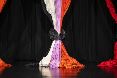 Voorstelling van gekleurde theatergordijnen in zwart, paars, wit, oranje en rood, samengebonden in het midden.