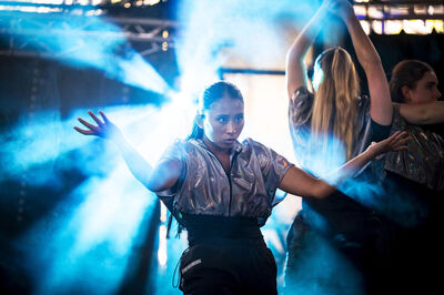 Twee danseressen in metallic outfits optreden met blauwe lichteffecten en rook op de achtergrond.