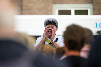 Een persoon in een uniform spreekt tot een groep mensen, met een nadruk op zijn woorden.