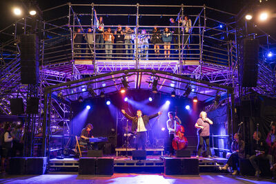 Een live optreden op een podium met muzikanten en zangers, omringd door een enthousiast publiek.