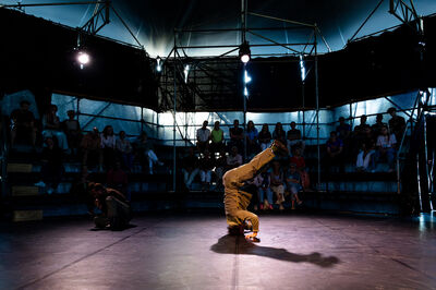 Een persoon breakdanced  in een donkere theatertent.