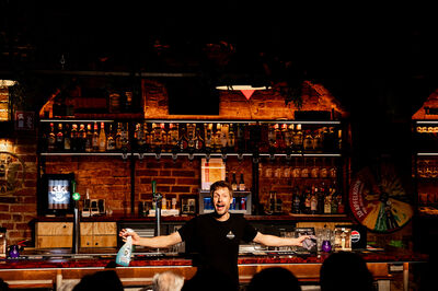 Man staat achter een bar in een cafe en speelt een voorstelling. 