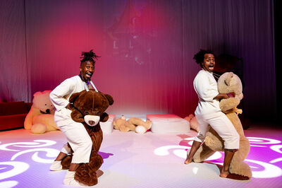Twee personen dansen in een voorstelling met twee grote teddyberen.
