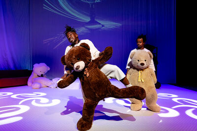 Twee personen dansen in een voorstelling met twee grote teddyberen.