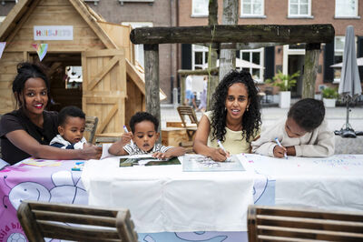 Drie kinderen zitten samen met twee moeders aan een lage tafel te tekenen.