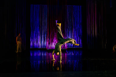 Een persoon danst en maakt hiervoor een handstand met de benen achter elkaar.