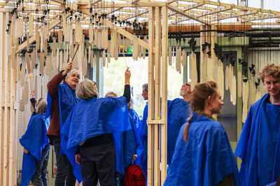 Mensen dragen blauwe capes en slaan met stokjes tegen hangers van klei.