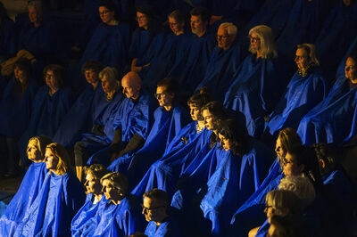 Publiek zit op een tribune en draagt blauwe capes.