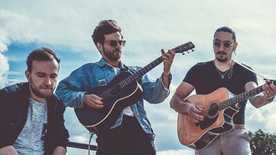 Een bandfoto van drie mensen. Twee personen spelen gitaar.