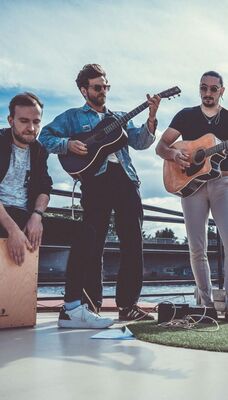 Een bandfoto van drie mensen. Twee personen spelen gitaar.