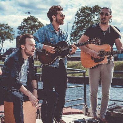 Een bandfoto van drie mensen. Twee personen spelen gitaar.