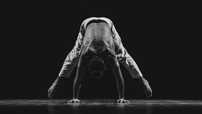 Een persoon doet een handstand en draagt alleen een broek.