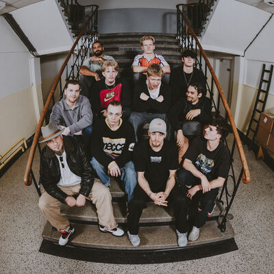Een groep breakdancers zit naast en onder elkaar op een trap in het trappenhuis van een oud gebouw.