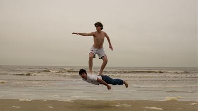 Foto van twee mensen op het strand. Een persoon gebruikt de ander als zwevend surfbord.