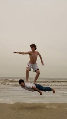 Foto van twee mensen op het strand. Een persoon gebruikt de ander als zwevend surfbord.