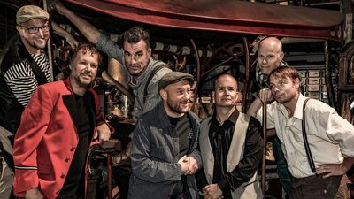 Een bandfoto van 7 muzikanten.