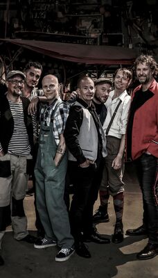 Een bandfoto van 7 muzikanten.