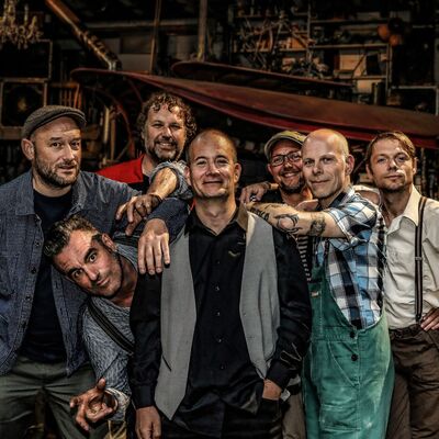 Een bandfoto van 7 muzikanten.