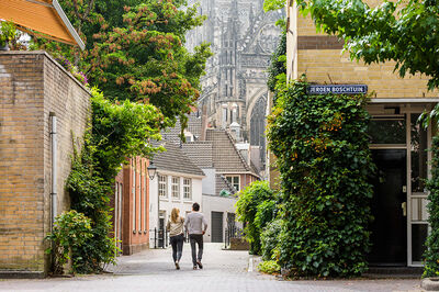 Personen lopen door een smalle straat richting de Sint Janskathedraal.