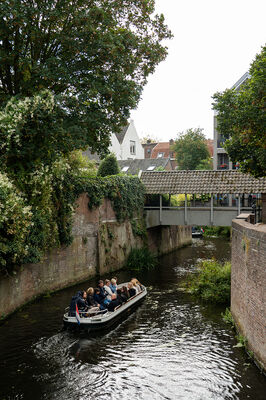 Een groep mensen zit op een boot die vaart door de gracht van de binnenstad van Den Bosch.