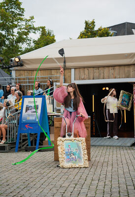 Een houten tent met daarvoor een acteur op een hometrainer en daaromheen lopen mensen.