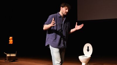 Foto van een man op theatervloer met naast hem een toilet.