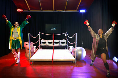 Twee boxers staan blij met de armen omhoog naast een boxring.