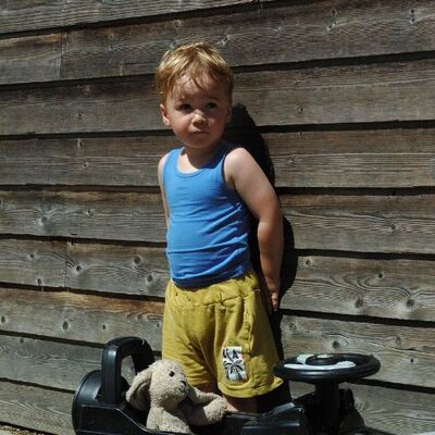 Een kind draagt zomerkleding en staat voor een houten schutting met een looptrein met konijnknuffel op de grond en een bordje met de tekst later wordt ik vrijwilliger.