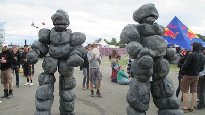 Twee stenen reuzen lopen op een festival tussen de mensen.