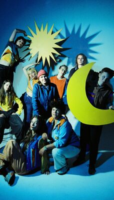 Een bandfoto met negen mensen. Sommigen houden een ster of maan vast.